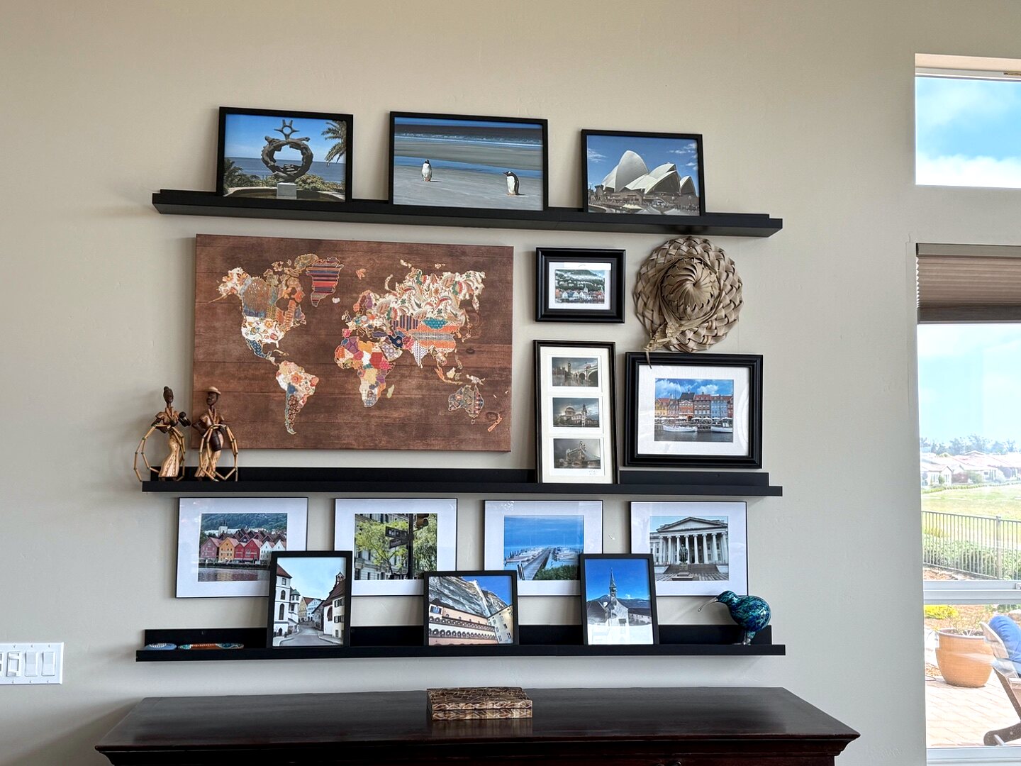 Living room travel gallery wall after redesign — three floating shelves with a world map and framed photographs