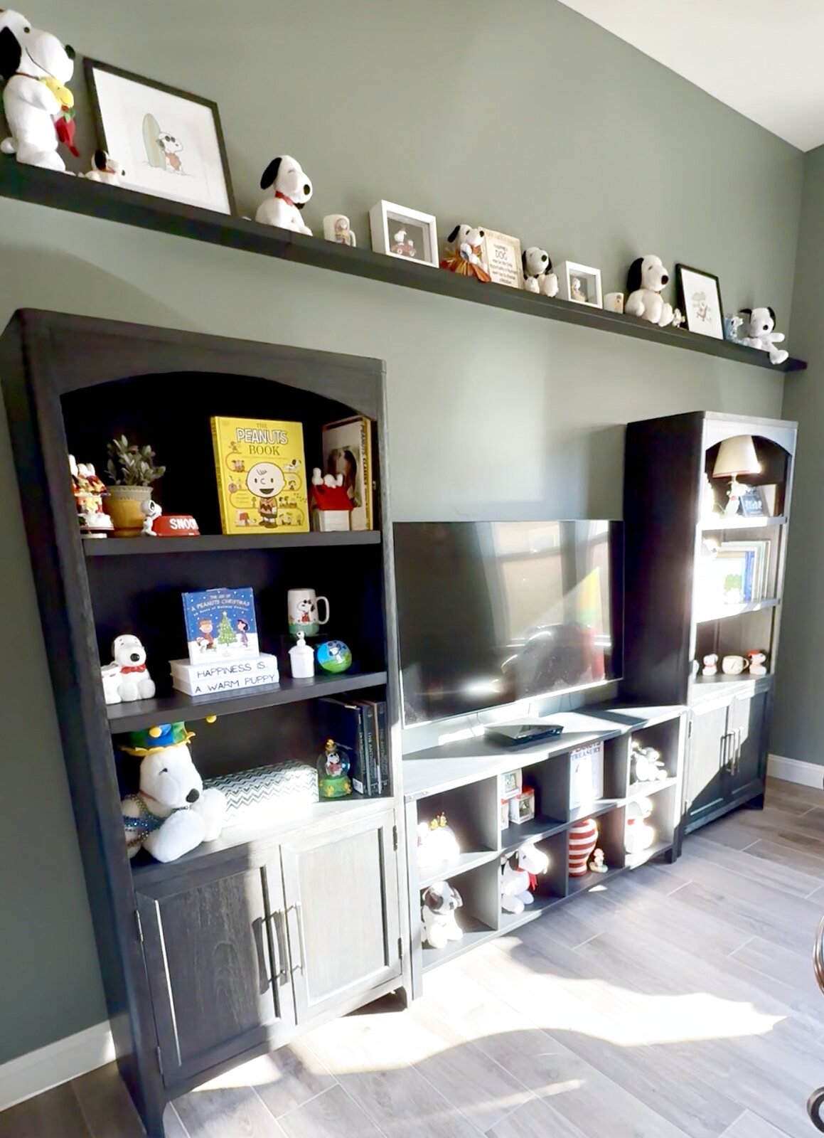 Snoopy room after — a completed media wall with display shelves full of Peanuts memorabilia on sage green walls