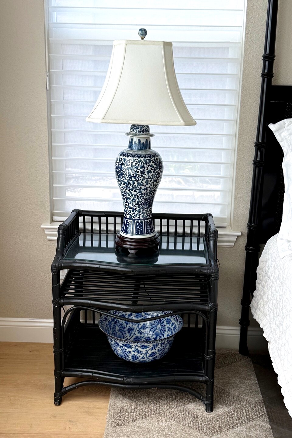 Nightstand vignette with a blue-and-white lamp and a matching bowl on a black rattan stand